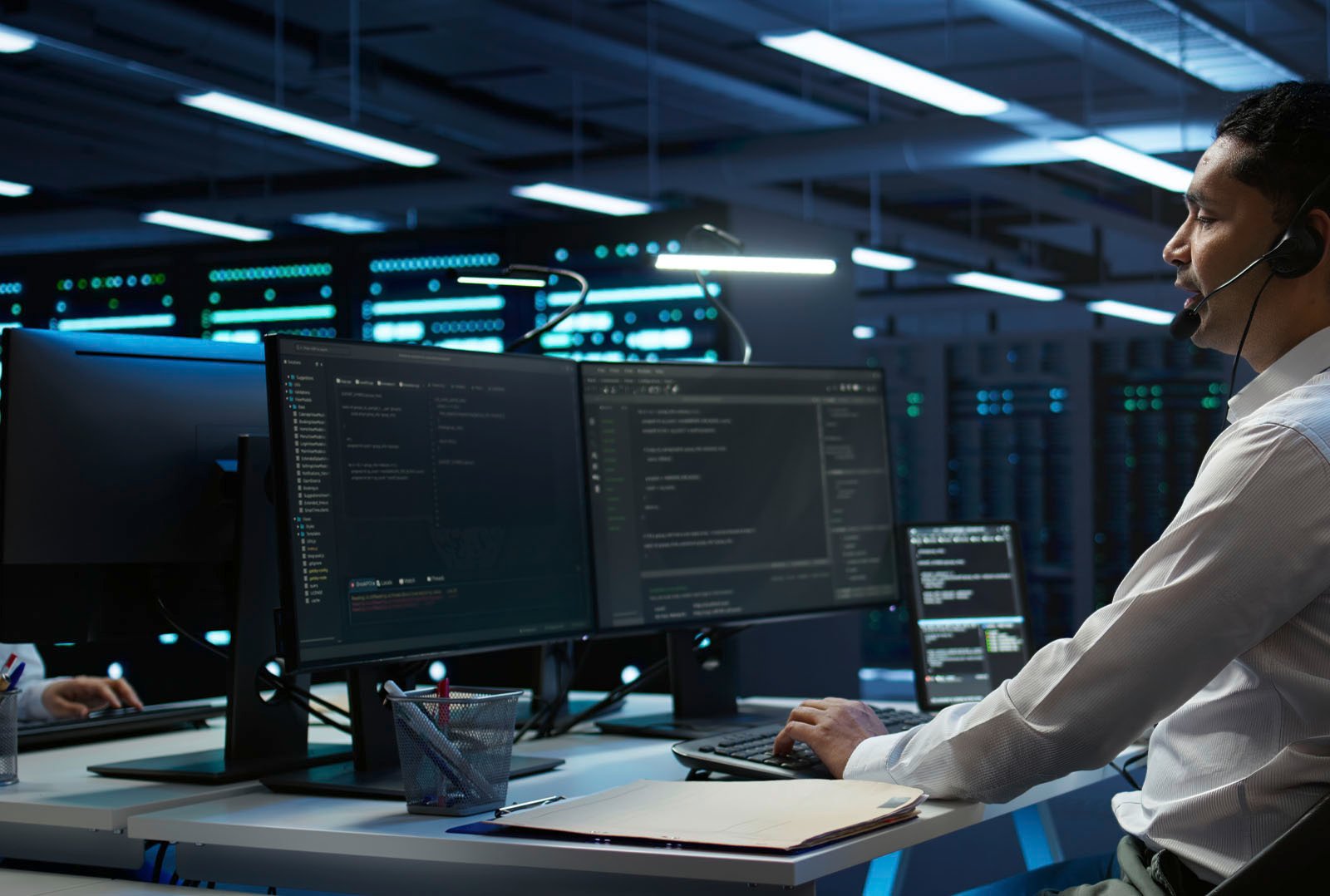 Fleet manager with headset monitors charging infrastructure at computer workstation in modern server room - symbol for central administration and remote maintenance of e-charging points in fleet management
