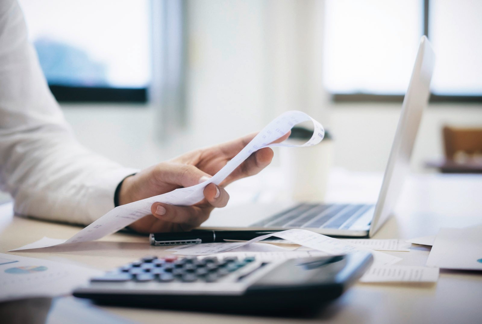 Person checks receipts in front of laptop with calculator - symbolic image for automated payment flow and digital billing in fleet management