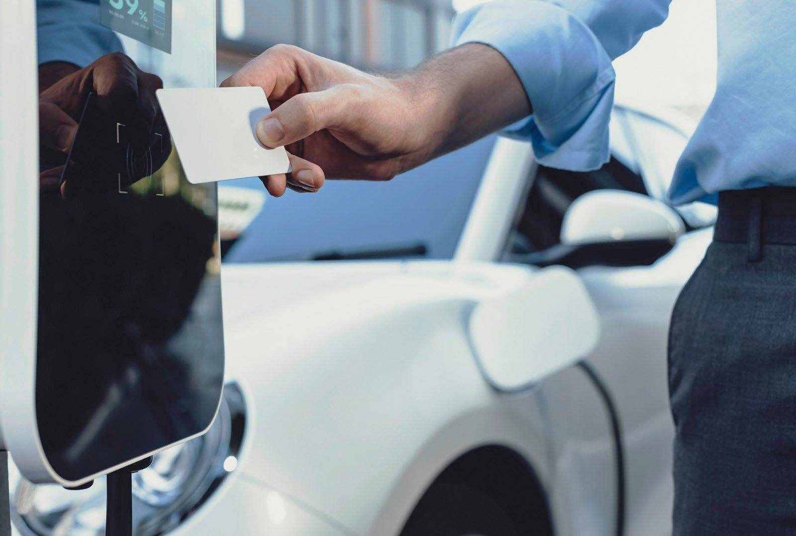 Man holds RFID card in front of charging station to start charging a white electric car - symbol of modern charging infrastructure at the company site