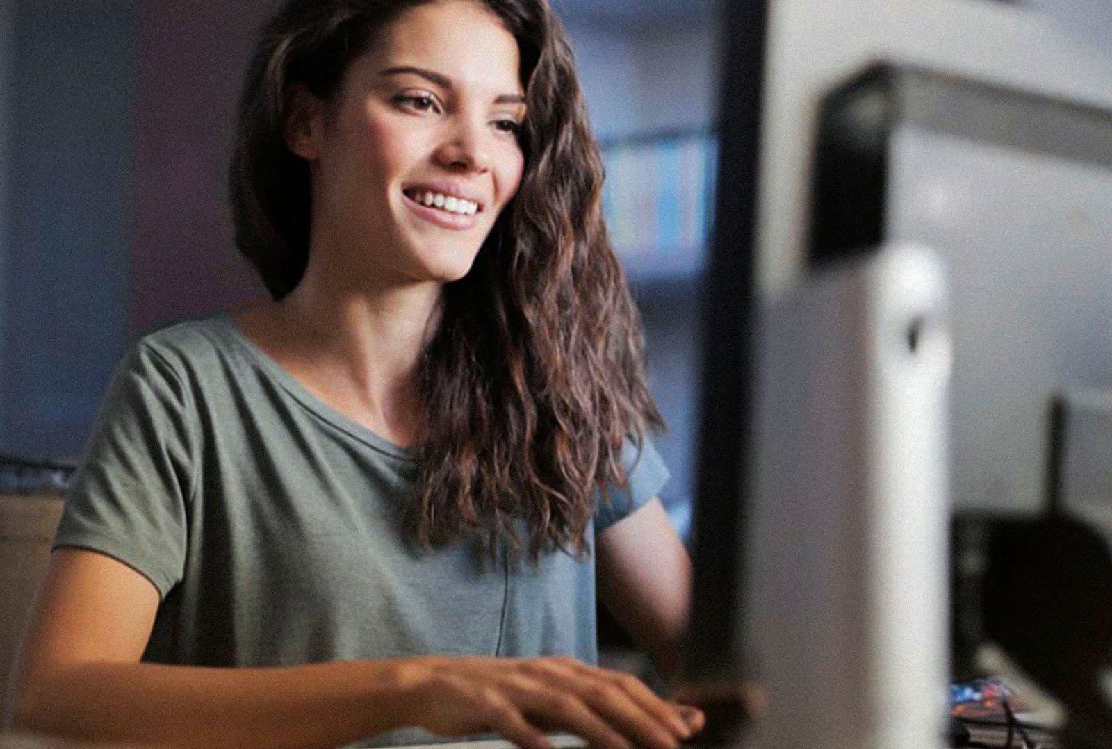 Smiling young woman sits at her desk and uses the e-mobilio store on her computer to order charging products such as wallboxes and accessories for her electric company car