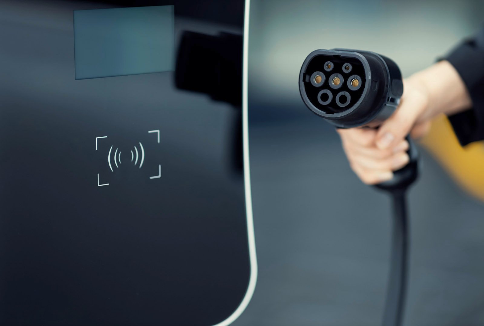 Close-up of a modern fast charger with RFID reader and a hand holding a charging cable - a symbol for DC charging solutions in car dealerships
