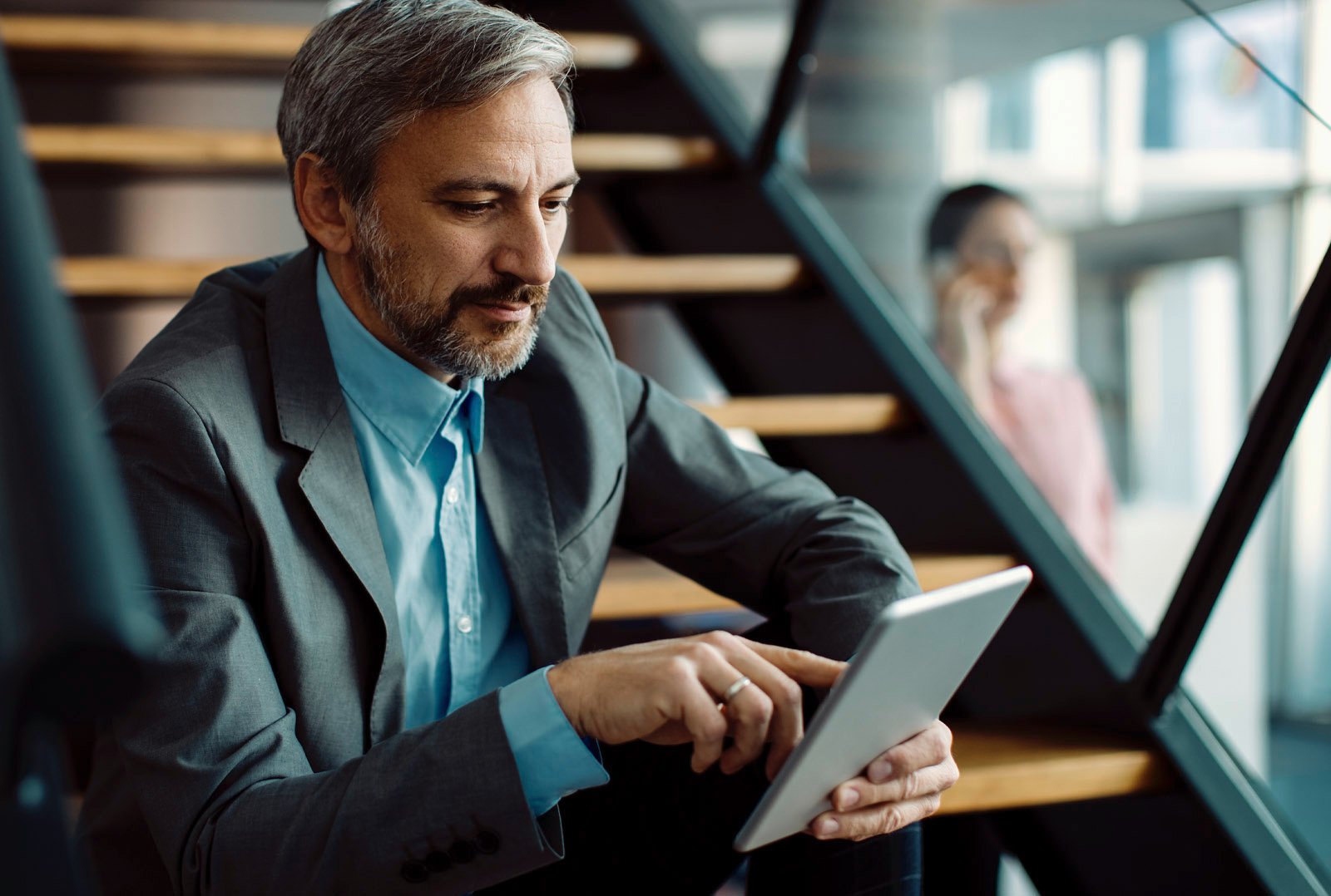 Businessman in gray suit using a tablet on a staircase in a modern office - stands for digital cross-selling automation and increased efficiency