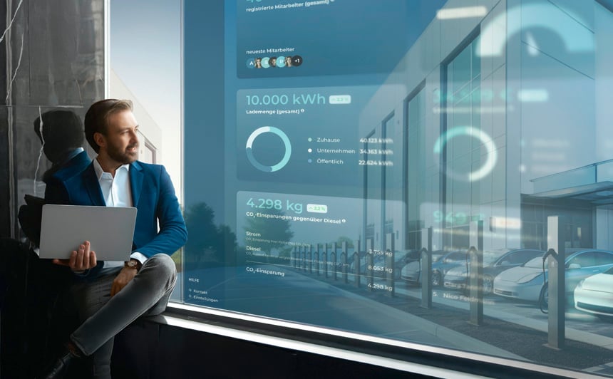 Man with laptop sitting in front of modern company headquarters with several parked e-cars and charging stations - symbolic image for holistic fleet electrification solutions in the commercial sector