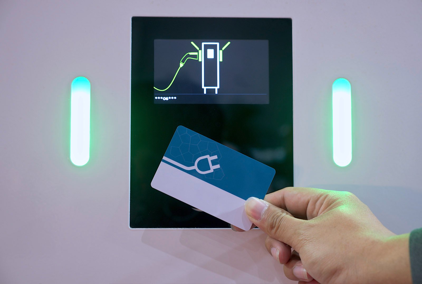 Hand holds charging card in front of a charger with display and green illuminated indicators - symbol for access to charging infrastructure via white label card