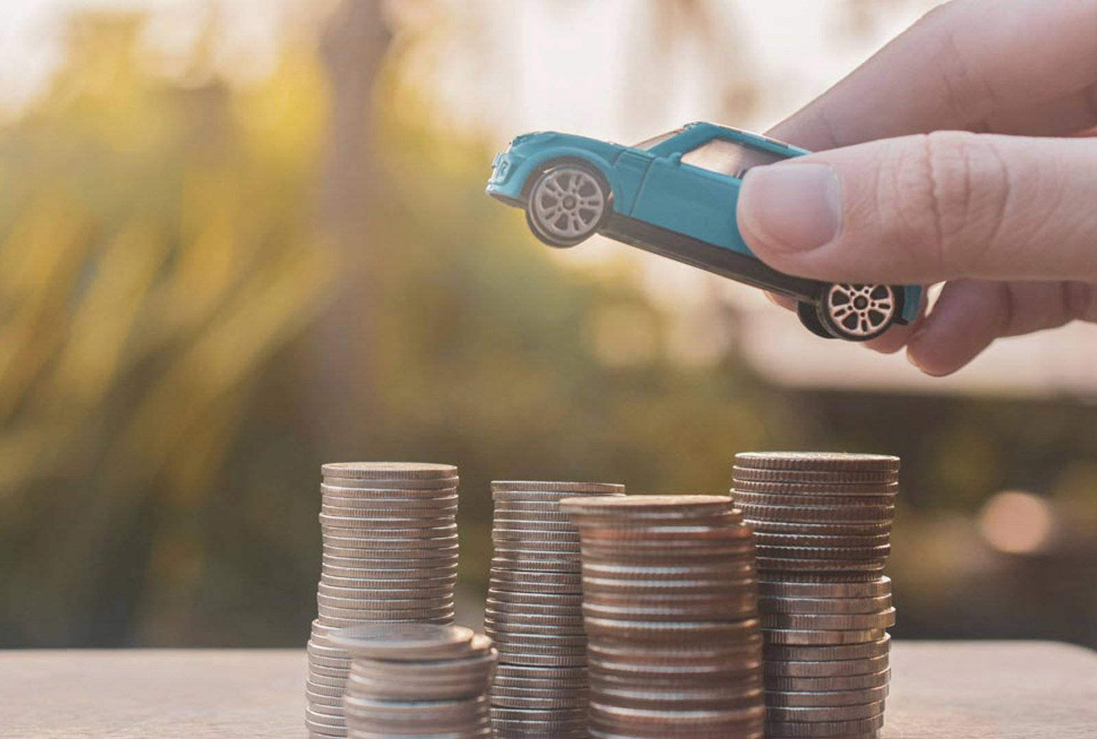 Hand places a blue toy car on a pile of coins - symbolizes financial benefits from the GHG bonus in the area of electromobility