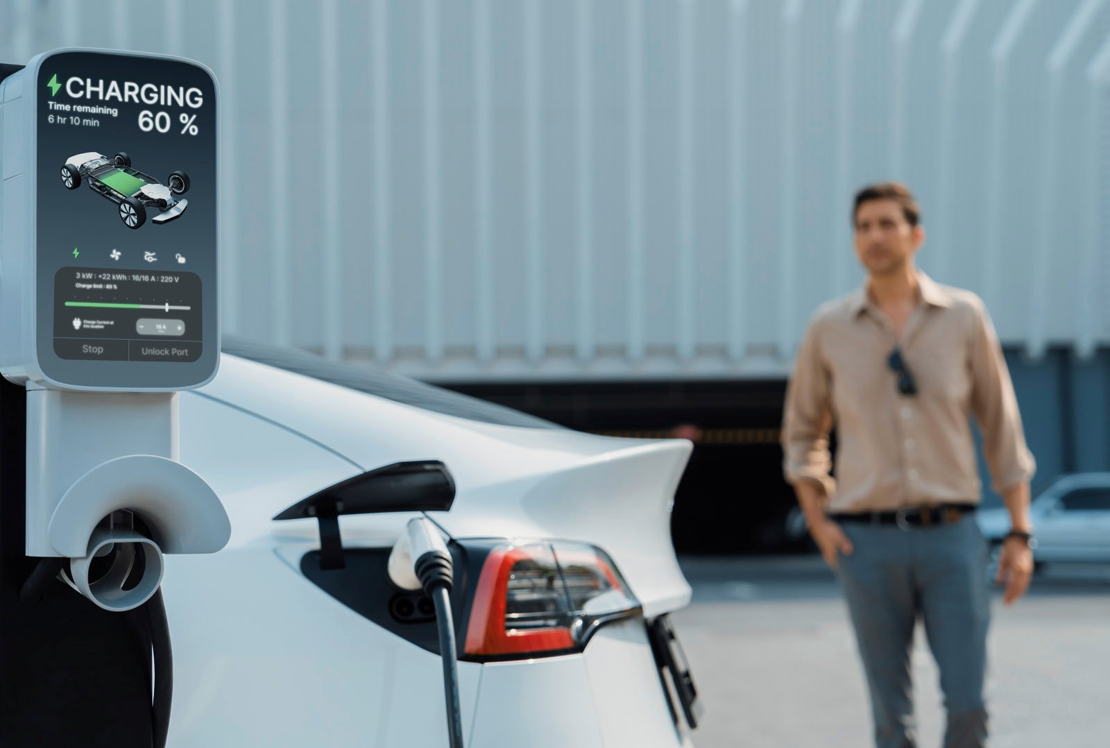 White electric car at DC fast charging station with digital display - a man stands in front of a modern building in the background