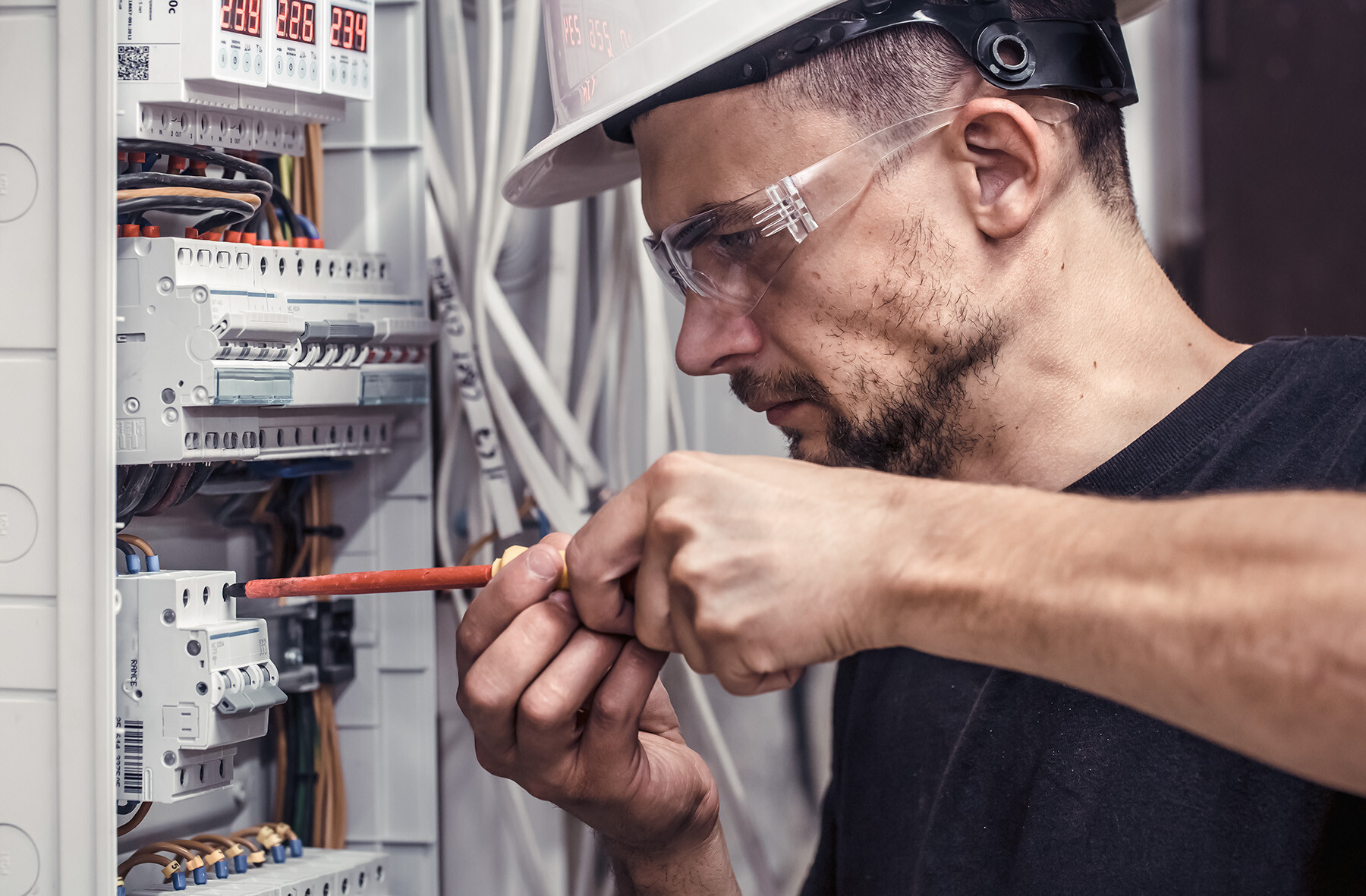 Electrician with safety goggles and helmet working on a fuse box - symbol for professional installation and maintenance of charging infrastructure in the corporate environment